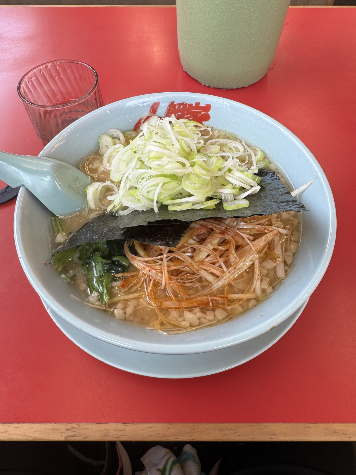 山岡家のラーメンの俯瞰写真。海苔の上に白ねぎが大盛り、その下に赤いピリ辛ねぎが乗っている。yagi が味付けねぎ多めとピリ辛指定の裏技を仕込んだ実物の一杯。
