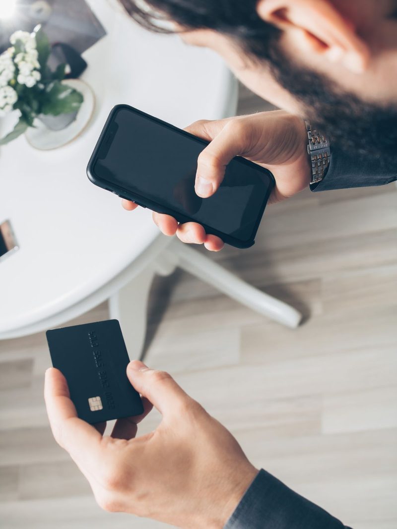 スマホとキャッシュカードを手に持つ場面、通帳をアプリに置き換える手続きを連想させる